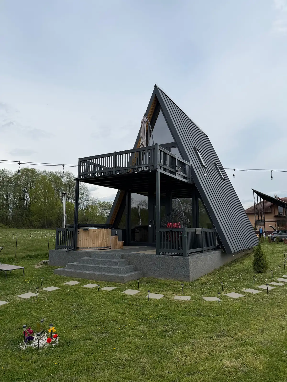 Cabana Ross-A, o cabană A-frame neagră cu ciubăr pe terasă, într-o poiană verde