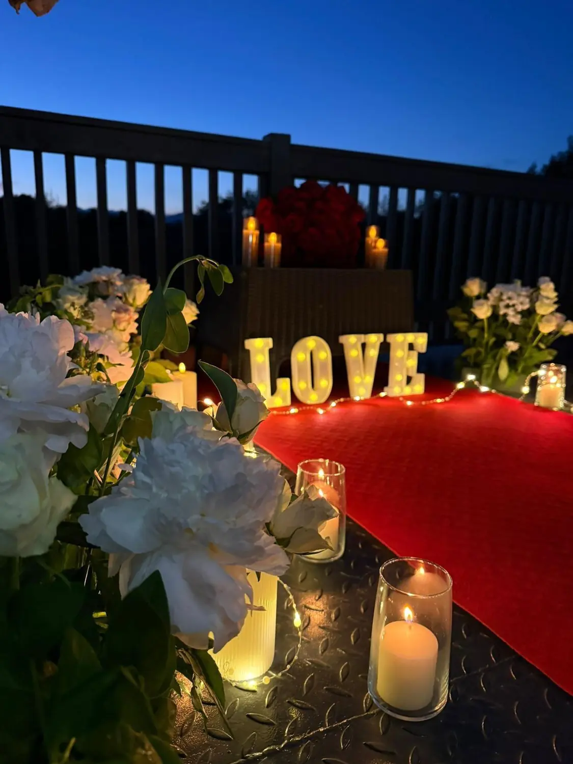 Aranjament romantic pe terasă, cu litere LOVE luminate, lumânări și trandafiri, la asfințit